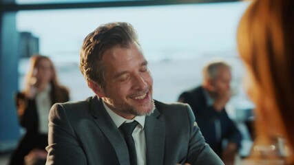 A smiling businessman in a suit engages in conversation at a venue overlooking an airport, enjoying the moment.
