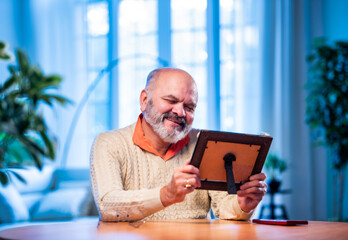 Elderly Indian man holding framed photo with love, lost in memory and emotion