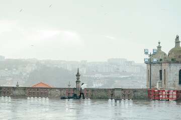 A traveler with an umbrella braves the rain on the Clerigos Church balcony, experiencing panoramic...
