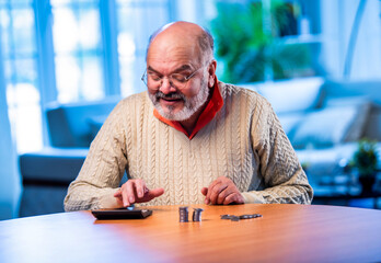 Old Indian man with coin stack and calculator managing money at home table
