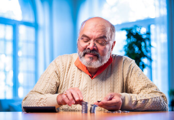 Old Indian man with coin stack and calculator managing money at home table