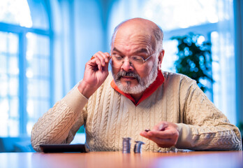 Old Indian man with coin stack and calculator managing money at home table