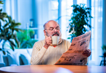 Senior Indian man with newspaper and tea at table during quiet morning routine at home