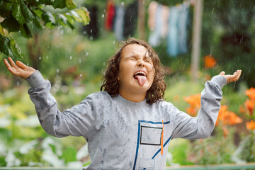 Cute happy child girl laughs and plays under summer rain in a garden