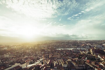 Sunlight illuminates the sprawling rooftops of Porto. The Douro River winds through the urban landscape, showcasing iconic landmarks and attracting diverse travelers