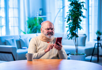Old Indian man with tea and smartphone browsing content during calm indoor morning