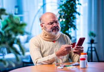 Old Indian man with smartphone and medicine pack verifying ingredients at home