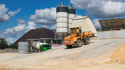 Construction activities involve heavy machinery working under a partly cloudy sky at a busy site