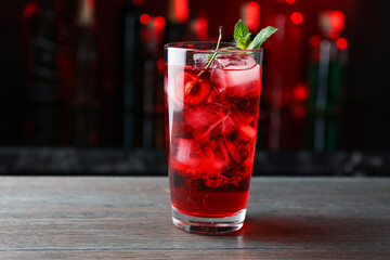 Tasty cherry soda water with ice cubes, berry and mint in glass on wooden table against blurred background, closeup