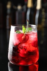 Tasty cherry soda water with ice cubes, berry and mint in glass on mirror table against blurred background, closeup