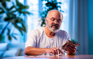 Elderly Indian man manages budget by counting cash and noting expenses at home