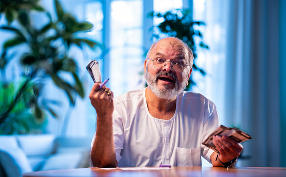 Elderly Indian man manages budget by counting cash and noting expenses at home