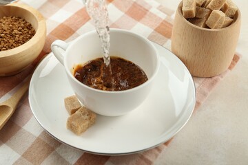 Pouring hot water into cup with instant coffee at light table, closeup