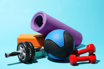 Medicine ball, ab wheel, foam blocks, fitness mat and dumbbells on light blue background