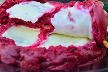 A close-up reveals the rich texture of a red velvet cake roll, generously filled and topped with creamy white frosting, hinting at its deliciousness