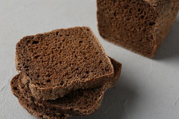 Pieces of fresh rye bread on light grey textured table, closeup