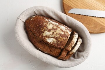 Fresh rye bread in basket on white textured table, flat lay