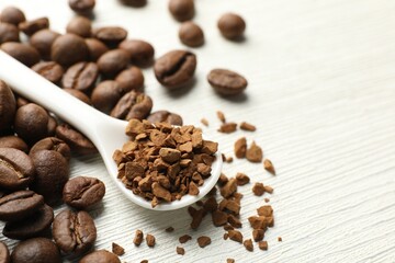 Spoon with granulated instant coffee and beans on white wooden table, closeup