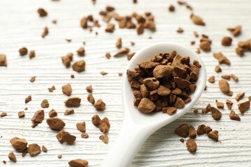 Spoon with granulated instant coffee on white wooden table, closeup