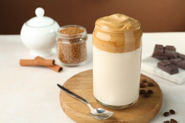 Delicious dalgona coffee in glass, beans, granules, chocolate and cinnamon on white table, closeup