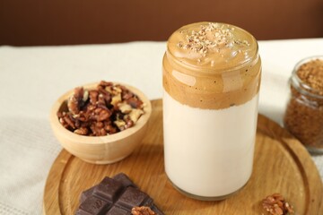 Delicious dalgona coffee in glass, pieces of chocolate, walnuts and granules on table, closeup