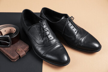 Pair of black leather shoes, purse and belt on color background, closeup