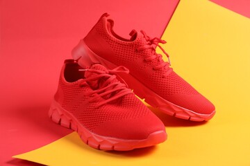 Pair of red sneakers on color background