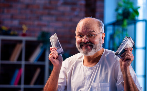 Elderly Indian man manages budget by counting cash and noting expenses at home