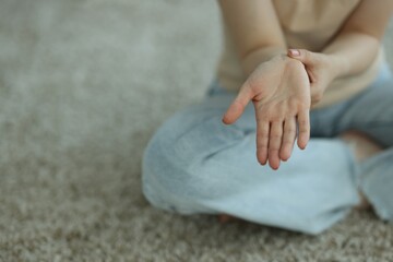 Woman suffering from wrist pain on floor at home, closeup. Space for text