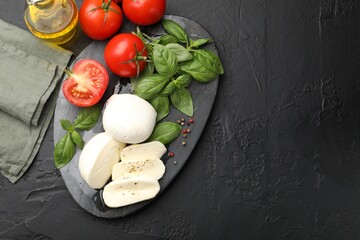 Tasty mozzarella cheese, tomatoes, basil and spices on black table, flat lay. Space for text