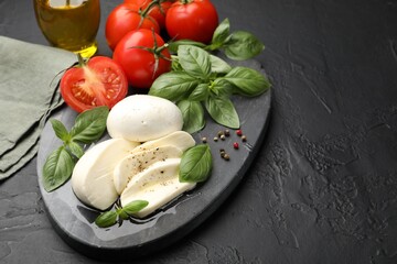 Tasty mozzarella cheese, tomatoes, basil and spices on black table, closeup. Space for text