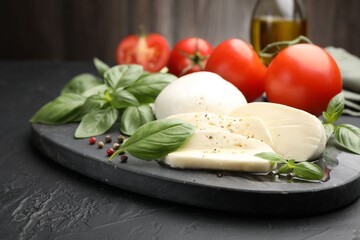 Tasty mozzarella cheese, tomatoes, basil, peppercorns and oil on black table, closeup