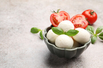 Tasty mozzarella cheese balls, tomatoes and basil on grey table, closeup. Space for text