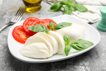 Tasty mozzarella cheese, tomato, basil and spices on grey table, closeup