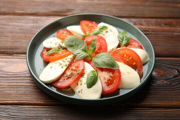 Tasty salad Caprese with mozzarella, tomatoes, basil and spices on wooden table, closeup