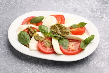 Tasty salad Caprese with mozzarella, tomatoes, basil and pesto sauce on grey table, closeup