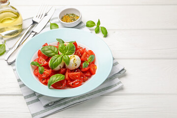 Tasty salad Caprese with mozzarella, tomatoes, basil and spices on white wooden table, closeup. Space for text