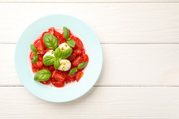 Tasty salad Caprese with mozzarella, tomatoes, basil and spices on white wooden table, top view. Space for text