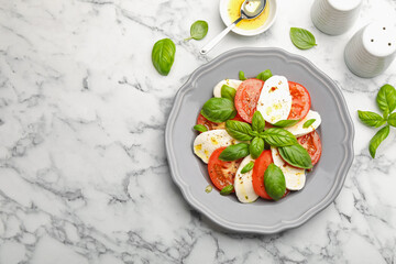 Tasty salad Caprese with mozzarella, tomatoes, basil and spices on white marble table, flat lay. Space for text