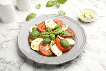 Tasty salad Caprese with mozzarella, tomatoes, basil and spices on white marble table, closeup