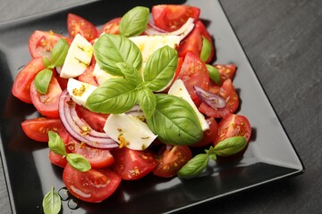 Tasty salad Caprese with mozzarella, tomatoes, basil, onion and spices on black table, closeup