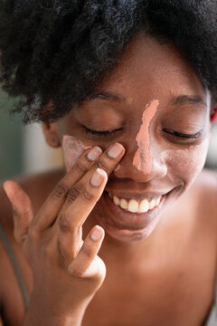 High angle of charming black female applying purifying mineral mask on face while doing everyday beauty procedure at home