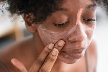 High angle of charming black female applying purifying mineral mask on face while doing everyday beauty procedure at home