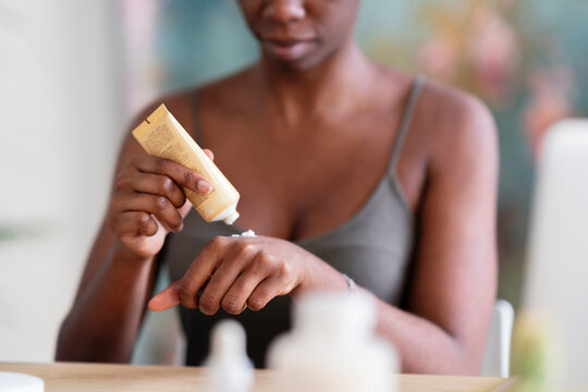 Unrecognizable crop black female applying hand cream and doing everyday beauty treatment at home
