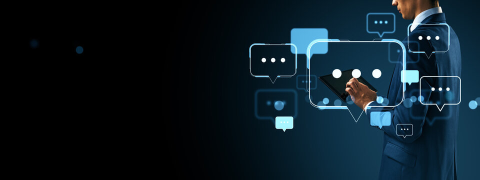 Businessman using tablet with digital chat bubbles representing online communication and social media interaction on dark background.