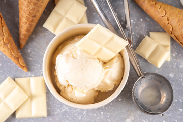 White chocolate ice cream. Portioned bowl with gourmet white chocolate gelato, cold creamy dessert, with ice cream cones and chocolate slices on table, copy space