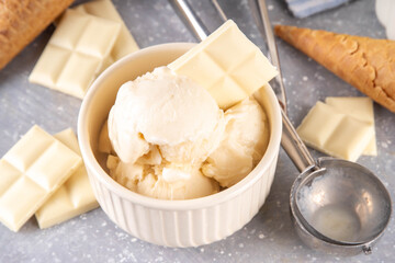 White chocolate ice cream. Portioned bowl with gourmet white chocolate gelato, cold creamy dessert, with ice cream cones and chocolate slices on table, copy space