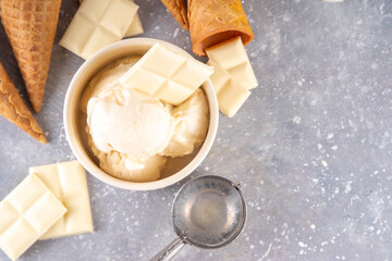 White chocolate ice cream. Portioned bowl with gourmet white chocolate gelato, cold creamy dessert, with ice cream cones and chocolate slices on table, copy space
