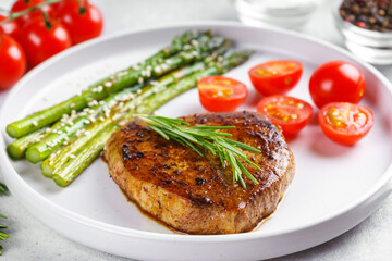 Close up, macro of tasty grilled beef steak served with green asparagus and cherry tomatoes on white plate, with cutlery. Perfect for food menu, diet, or culinary design concepts.