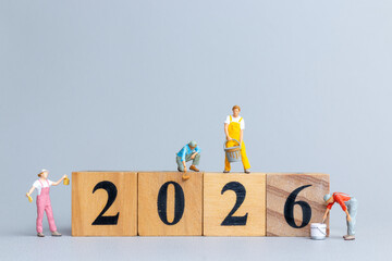 Tiny figurine workers painting and assembling wooden blocks to form the number 2026